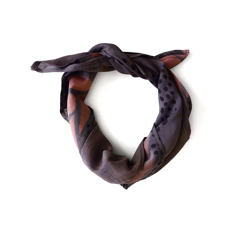 K&ouml;nnte beinhalten: Ein dunkelgraues Bandana mit Knoten. Es zeigt ein Muster aus braunen und schwarzen Formen und Punkten. Der Stoff wirkt weich und leicht, geeignet f&uuml;r verschiedene Styling-Optionen. Ein vielseitiges Accessoire.