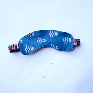 May include: A blue sleep mask with a white geometric pattern. The mask has an elastic band for a comfortable fit.