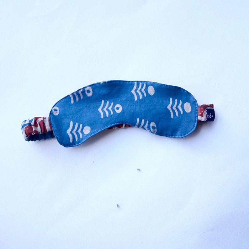 May include: A blue sleep mask with a white geometric pattern. The mask has an elastic band for a comfortable fit.