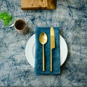 May include: A blue linen napkin with a gold knife and spoon on a white plate. The plate is on a blue and white patterned tablecloth.