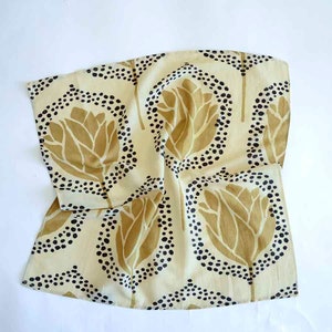 May include: A cream-colored cotton tea towel with a repeating pattern of stylized gold flowers outlined in black dots.
