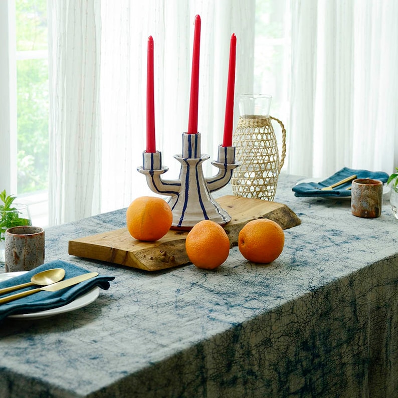 May include: A white ceramic candle holder with blue stripes and three red candles. The candle holder is on a wooden board with three oranges.