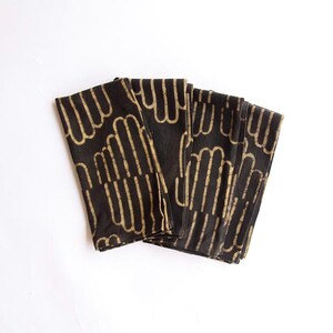 May include: Set of six black cotton napkins with a gold geometric pattern. The napkins are folded and stacked on a white background.