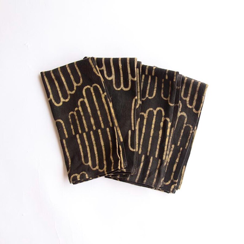 May include: Set of six black cotton napkins with a gold geometric pattern. The napkins are folded and stacked on a white background.