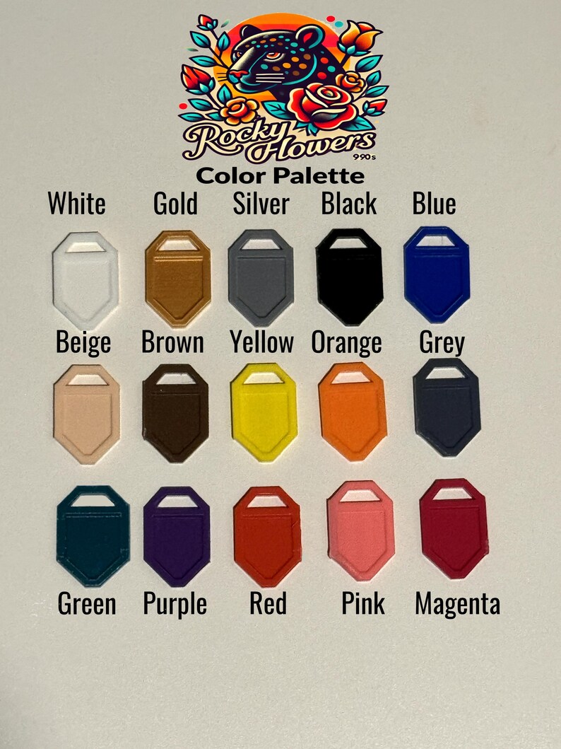 May include: A colour palette chart featuring fifteen shield-shaped tags in various colours including white, gold, silver, black, blue, beige, brown, yellow, orange, grey, green, purple, red, pink, and magenta, with the text Rocky Flowers 990s.