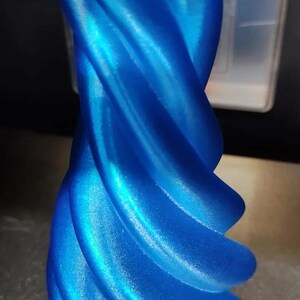 Op de afbeelding: Een levendige blauwe, spiraalvormige vaas met een glanzende afwerking. De vaas heeft een uniek, gedraaid ontwerp, met een reeks gebogen ribbels. Het object is waarschijnlijk 3D-geprint en de kleur is een helder, opvallend blauw.