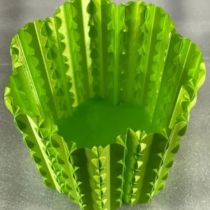 Op de afbeelding: Een felgroene, 3D-geprinte plantenbak met een uniek, getextureerd ontwerp. De plantenbak heeft een gegolfde, geschulpte rand en een reeks ruitvormige uitsparingen langs de zijkanten. De binnenkant is effen, glad groen.