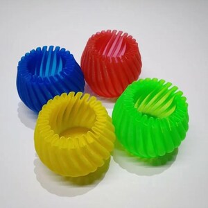 Può includere: Quattro oggetti sferici colorati con un design a spirale. Gli oggetti sono blu, rossi, verdi e gialli. Hanno un centro cavo con un interno a coste. Gli oggetti sono su una superficie bianca.