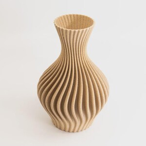 Op de afbeelding: Een beige decoratieve vaas met een uniek, geribbeld ontwerp. De vaas heeft een brede, afgeronde basis die taps toeloopt naar een smalle hals en een uitlopende opening. De verticale ribbels creëren een textuurachtig, golfachtig patroon.