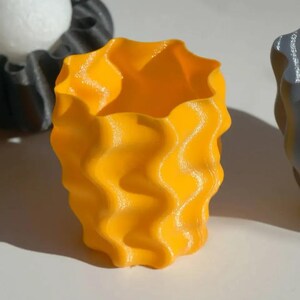 May include: Three decorative vases with wavy edges are shown. The central vase is bright yellow, with black and grey vases on either side. The vases have a textured, rippled design. These vases are suitable for home decor.