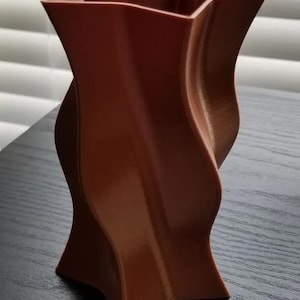 Könnte beinhalten: Eine braune, sternförmige Vase mit einem gedrehten Design. Die Vase hat eine glänzende Oberfläche und steht auf einer dunklen Oberfläche. Die Vase ist etwa 20 cm hoch.