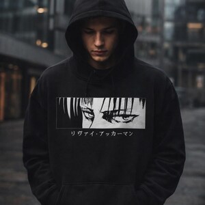 May include: Black hooded sweatshirt with a graphic of anime eyes and the Japanese text "リヴァイ・アッカーマン" in a white rectangle. The sweatshirt has a drawstring hood and a kangaroo pocket.