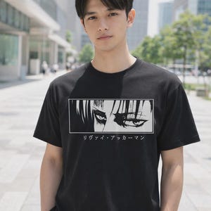 May include: Black crew neck t-shirt with a graphic of stylized eyes in a white rectangle, and Japanese text beneath. The t-shirt is a classic fit.