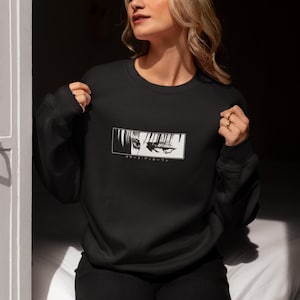 May include: Black crew neck sweatshirt with a white graphic of anime eyes in a rectangular frame. Japanese text is below the graphic. The sweatshirt is made of a soft material.