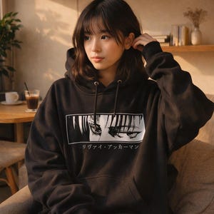 May include: Black hoodie featuring a white graphic of anime eyes and Japanese text. The hoodie has a drawstring hood and long sleeves. The graphic is rectangular and centered on the front.
