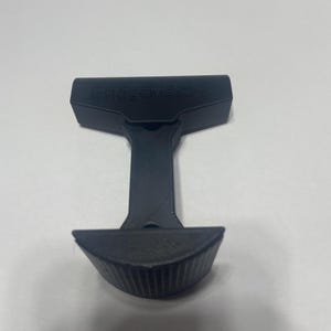 May include: Black plastic BridgeMate+ phone holder with a textured base and a top that can be used to hold a phone.