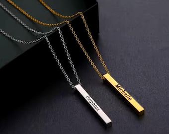 May include: Two gold bar necklaces with personalized names. The top necklace has the name "Michelle" engraved on the bar and the bottom necklace has the name "Delphine" engraved on the bar.