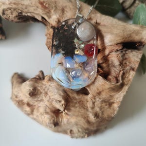 May include: A silver chain necklace with a rectangular pendant filled with various colorful stones and crystals, including blue, red, white, and black.