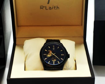 May include: A black watch with a gold face and a palm tree logo. The watch is in a black box with a gold interior and the brand name "R'Laith" printed on the inside of the lid.