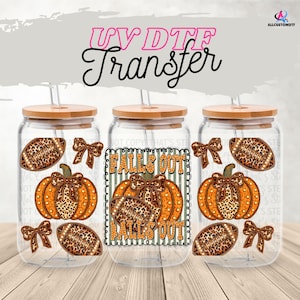 May include: Three glass tumblers with bamboo lids and straws. Each tumbler features a pumpkin and football design with leopard print accents. The text "FALLS OUT" is displayed on the center tumbler. The image is labeled "UV DTF Transfer".
