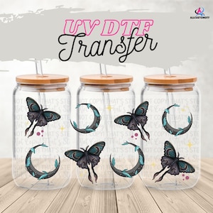 Puede incluir: Vasos de vidrio transparente con tapas y pajitas de bambú. Cada vaso presenta un diseño de mariposa y media luna. El texto "UV DTF Transfer" está en la parte superior.