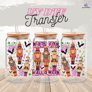 Puede incluir: Tres vasos de vidrio transparente con tapas y pajitas de madera. Cada vaso presenta un diseño de Halloween con ilustraciones de cascanueces coloridos, murciélagos, telarañas y el texto "Nuts for Halloween".