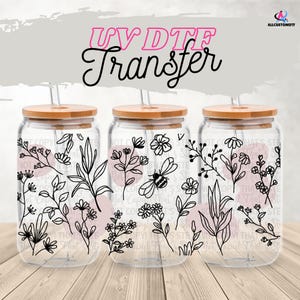 Puede incluir: Tres vasos de vidrio transparentes con tapas de bambú y pajitas. Cada vaso presenta un diseño floral en blanco y negro con una abeja en uno de los vasos. El texto "UV DTF Transfer" está en la parte superior de la imagen.