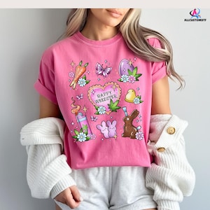 May include: Pink t-shirt with a graphic print of a heart with the text "Happy Weedster" and other Easter-themed illustrations, including a bunny, a carrot, a butterfly, and a Peep.