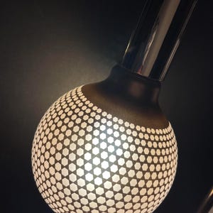 May include: A black and white patterned lampshade with a chrome base. The lampshade is a sphere with a geometric pattern of white hexagons on a black background.
