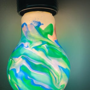May include: A decorative light bulb with a black base. The bulb is painted with swirling patterns of blue, green, white, and peach colors. The light bulb is a unique and artistic home decor item.