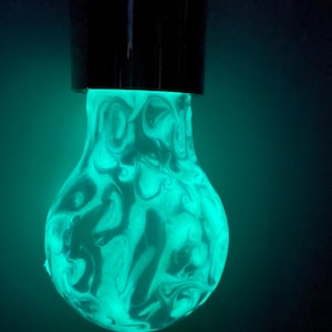 May include: A glowing light bulb with a black base. The bulb emits a bright teal light, with a swirling, marbled pattern in shades of white and teal. The background is a dark teal.