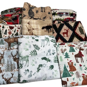 May include: A collection of folded fabric pieces with various nature-themed patterns. Designs include deer, rabbits, bears, trees, and hunting scenes. Colors range from neutral tones to reds and greens, creating a rustic and outdoorsy aesthetic.