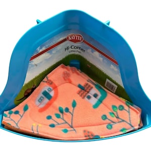 May include: A blue corner litter pan with a patterned pink fleece liner. The liner features a design of houses and foliage in teal, orange, and white. The packaging reads "Kaytee Hi-Corner Litter Pan".