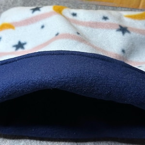 May include: A small pet bed with a navy blue rim and a white interior patterned with pink stripes, yellow accents, and dark blue stars. The bed is made of soft fleece material.