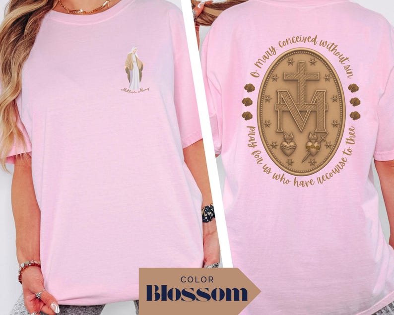 May include: A light pink t-shirt featuring a small illustration of a religious figure on the front. The back of the shirt displays a detailed emblem with text that reads "O Mary conceived without sin, pray for us who have recourse to thee."