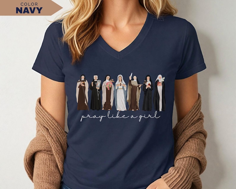 Op de afbeelding: Marineblauwe V-hals T-shirt met een rij ge&iuml;llustreerde religieuze figuren. De figuren zijn gekleed in verschillende gewaden. De zin "pray like a girl" is in cursief geschreven. Het T-shirt is effen marineblauw.
