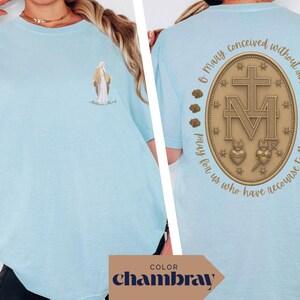 May include: Light blue t-shirt with a graphic on the front of a religious figure and the words "Mother Mary". The back of the shirt features a gold emblem with a cross, the letters "M" and "V", and the words "O Mary conceived without sin, pray for us who have recourse to thee."
