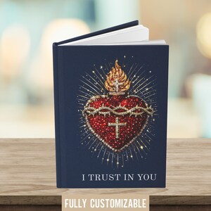 May include: A navy blue journal with the text "I TRUST IN YOU" and "FULLY CUSTOMIZABLE". The cover features a detailed illustration of a red heart with a crown of thorns, a cross, and a golden flame.