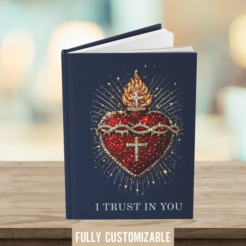 May include: A navy blue journal with the text "I TRUST IN YOU" and "FULLY CUSTOMIZABLE". The cover features a detailed illustration of a red heart with a crown of thorns, a cross, and a golden flame.