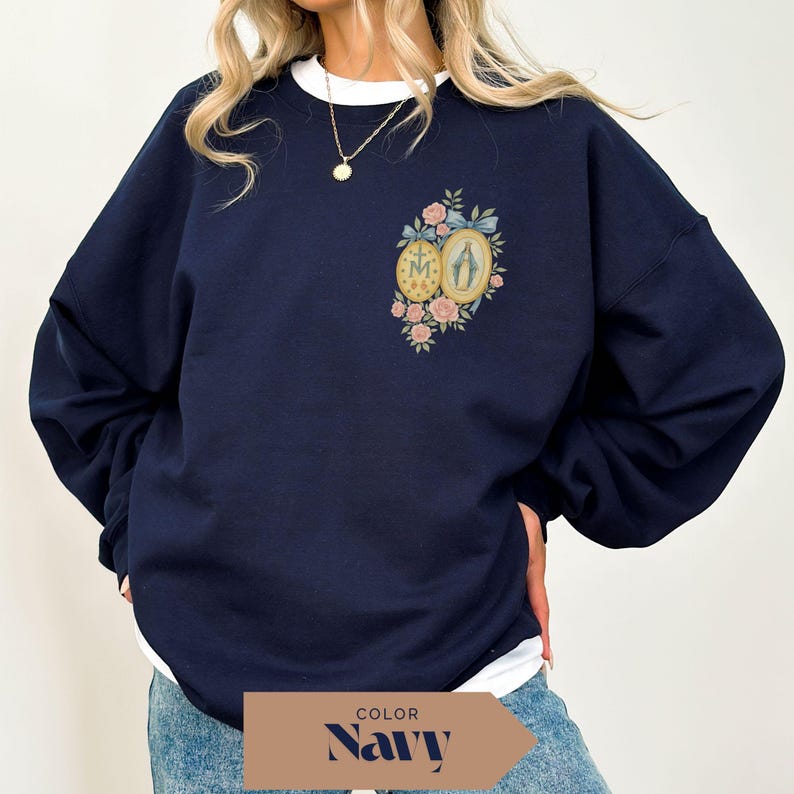 May include: Navy blue sweatshirt with a white crew neck collar. The front features a floral design with two oval medallions and the text "M" and "A". The design includes pink roses and a blue ribbon.