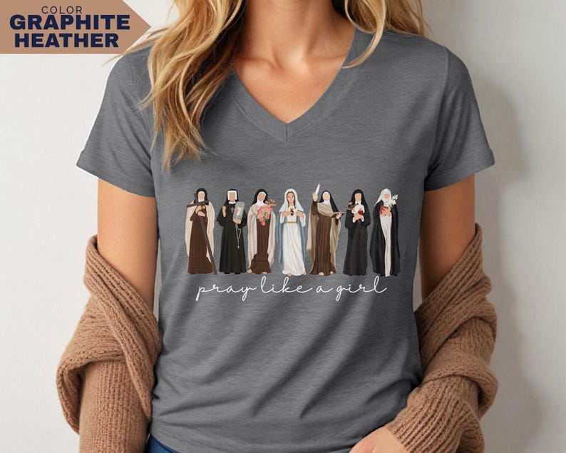 Op de afbeelding: Grafietkleurig V-hals T-shirt met een illustratie van religieuze figuren. De tekst "pray like a girl" staat in cursief onder de figuren. Het shirt heeft een neutrale grijze kleur.