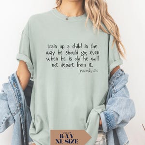 May include: A light green t-shirt with the text "train up a child in the way he should go; even when he is old he will not depart from it. Proverbs 22:6" in black. The shirt is a relaxed fit.