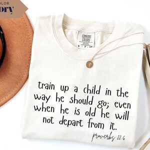 May include: Ivory-colored t-shirt with the text "train up a child in the way he should go; even when he is old he will not depart from it. Proverbs 22.6." A gold necklace is draped on the shirt.