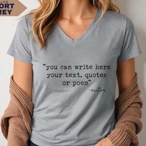 May include: A sport grey V-neck t-shirt featuring black typewriter-style text that reads: "you can write here your text, quotes or poem" followed by "-autor" on the next line. The shirt has short sleeves and a simple, clean design.