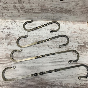 May include: Four twisted metal hooks in a bronze finish. The hooks are different lengths and are arranged in a staggered pattern on a white wooden surface.