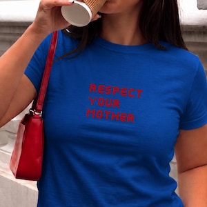 May include: A royal blue crop top with the text "RESPECT YOUR MOTHER" in red. The model is wearing black pants and a red purse. The word "royale" is printed in white on the bottom right.