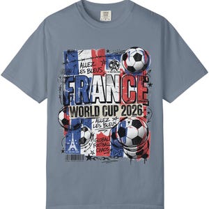 May include: A light blue t-shirt featuring a graphic design for the France World Cup 2026. The design includes the French flag, soccer balls, and the Eiffel Tower. Text includes "FRANCE", "WORLD CUP 2026", "Allez Les Bleus", and "Global Football Chaos".