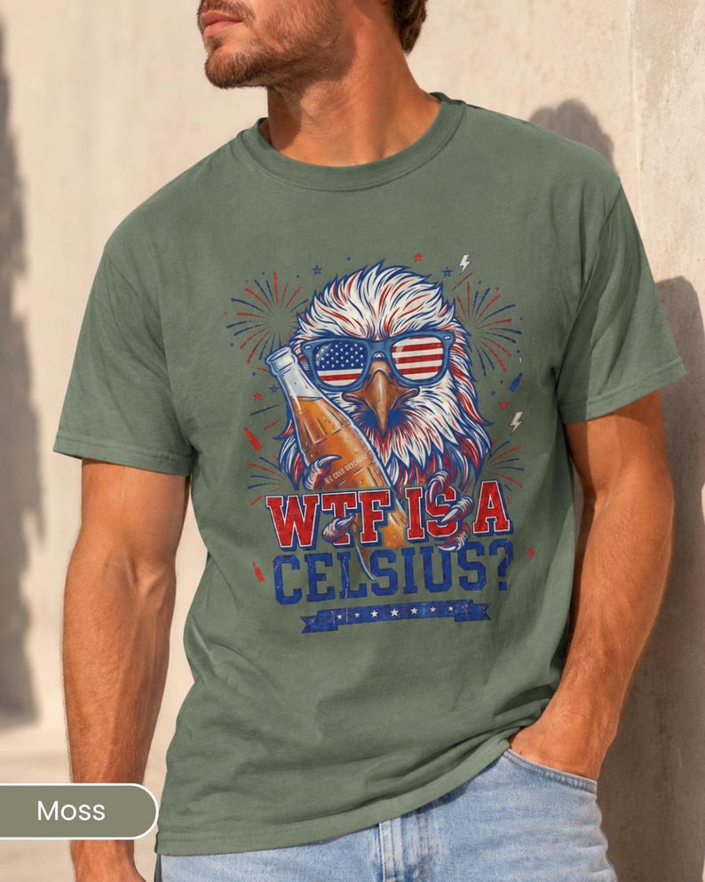 May include: A moss green short-sleeve t-shirt featuring a graphic of a bald eagle wearing American flag sunglasses and holding a beer bottle. The text reads "WTF IS A CELSIUS?" in red and blue lettering, surrounded by firework illustrations.