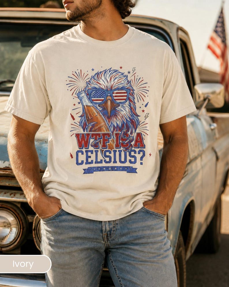 May include: An ivory short-sleeve t-shirt featuring a graphic of a bald eagle wearing American flag sunglasses and holding a glass bottle. The design includes red and blue fireworks, lightning bolts, and the text "WTF IS A CELSIUS?" in bold.
