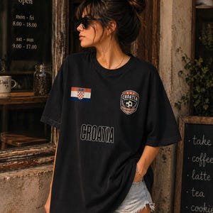 May include: Black t-shirt with the word "CROATIA" printed across the front. The shirt features the Croatian flag and a soccer emblem. The image also shows a cafe's open hours.